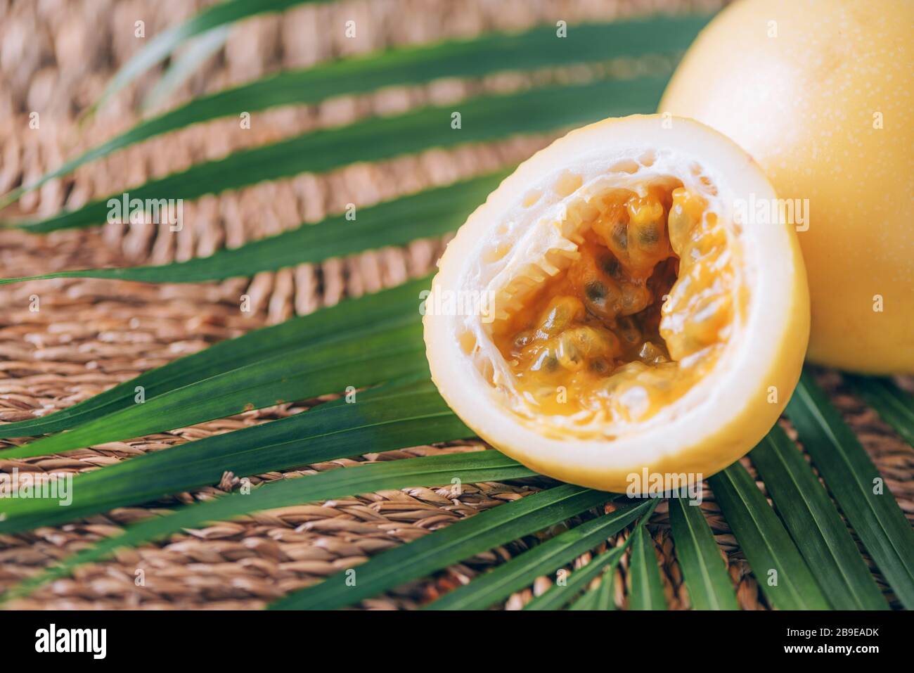 Gelbe Maracuya mit Palmblättern auf Rattanhintergrund. Kopierbereich. Passionsfrucht. Banner für kreatives Design. Sommerzeit. Tropische Reise, exotische Früchte. Stockfoto