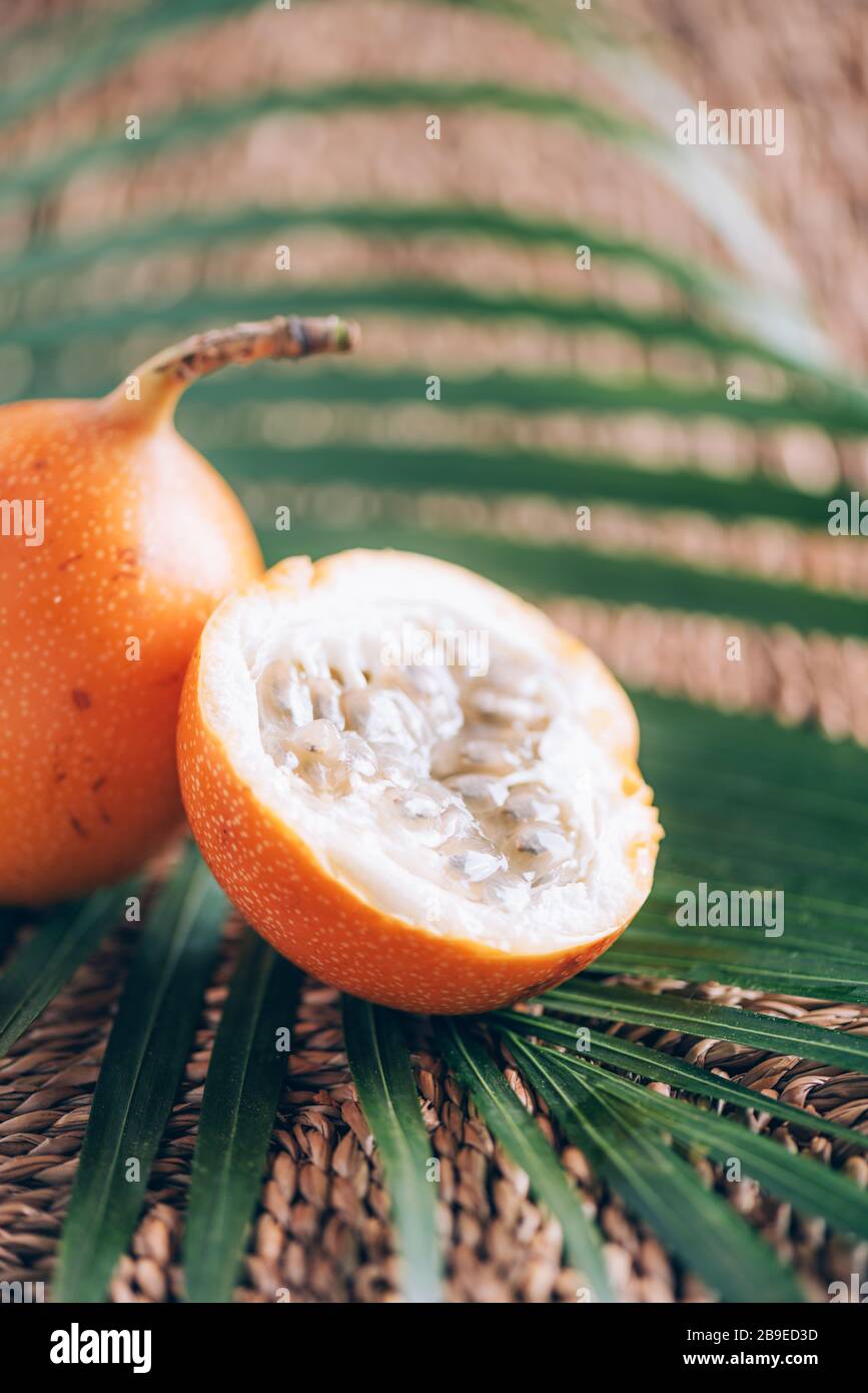 Süße Granadilla oder Granadia mit Palmblättern auf Rattanhintergrund. Kopierbereich. Banner für kreatives Design. Sommerzeit. Exotische Küche, tropische Obstkonce Stockfoto