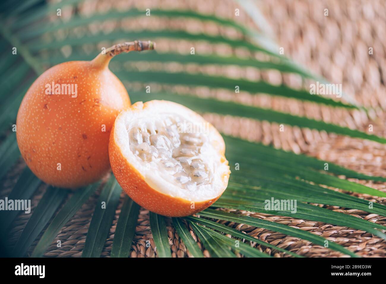 Süße Granadilla oder Granadia mit Palmblättern auf Rattanhintergrund. Kopierbereich. Banner für kreatives Design. Sommerzeit. Exotische Küche, tropische Obstkonce Stockfoto