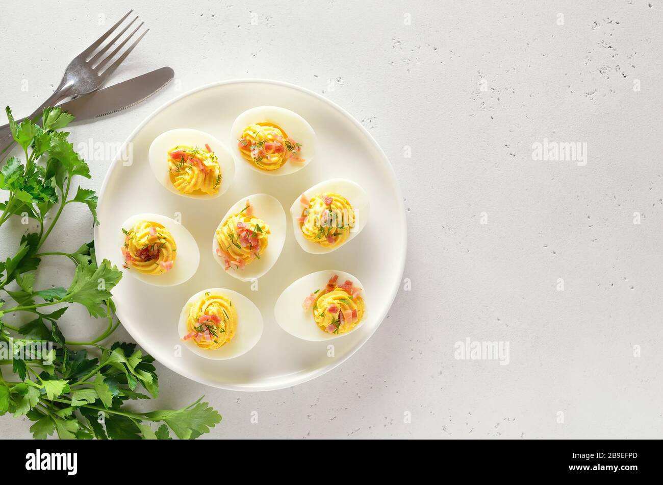 Gefüllte Eier mit Eigelb, Speck, Senf auf Platte über hellem Steinhintergrund mit freiem Textbereich. Gesunde Ernährung zum Frühstück. Draufsicht, flach Stockfoto