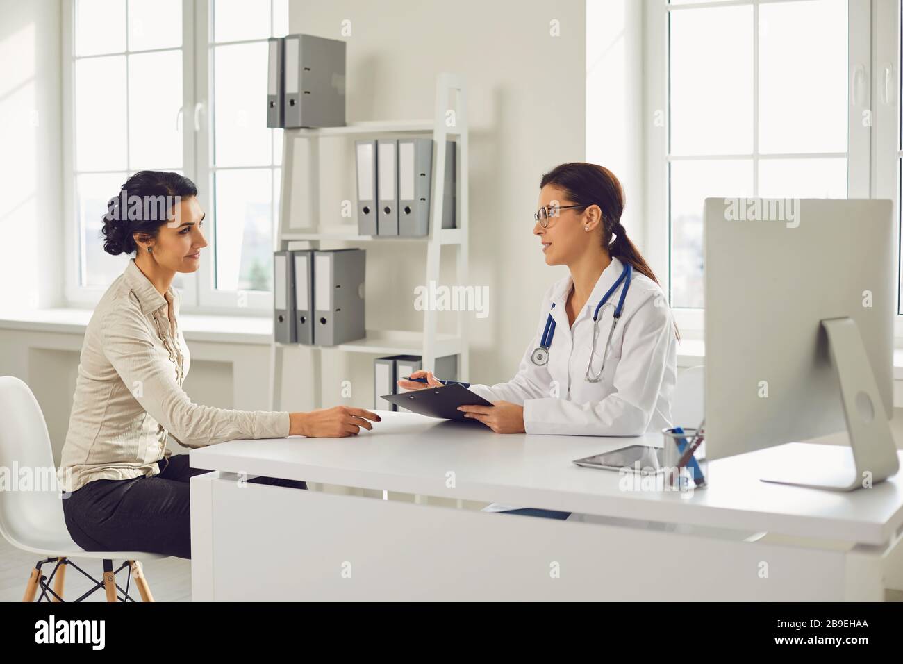 Ärztin Kinderärztin Gynäkologe spricht Klientin, die an einem Tisch in einer Klinik sitzt. Stockfoto