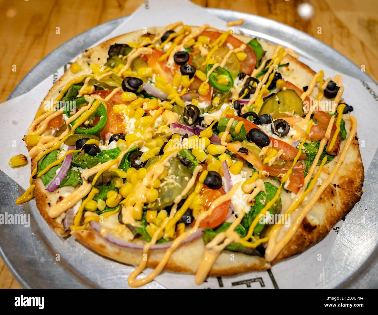 Pizza mit schwarzen Oliven, jalapeños, Spinat, goldenem Mais, Pickeln, Zwiebeln und Tomaten Stockfoto