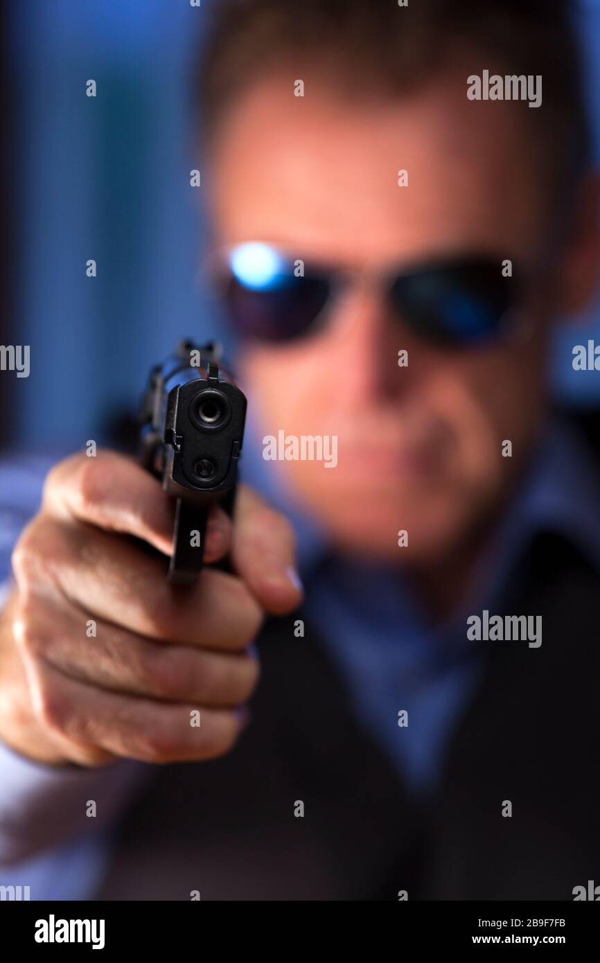Krimineller Geschäftsmann, der eine Pistole A auf den Betrachter zielt - dunkelblaues Bild Stockfoto