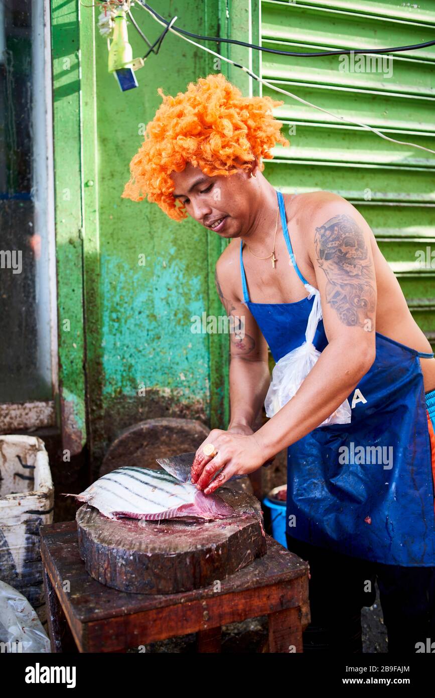 Fischhändler mit einer lustigen orangefarbenen Perücke, die Fisch auf den Straßen des öffentlichen Marktes Carbon verkauft. Stockfoto