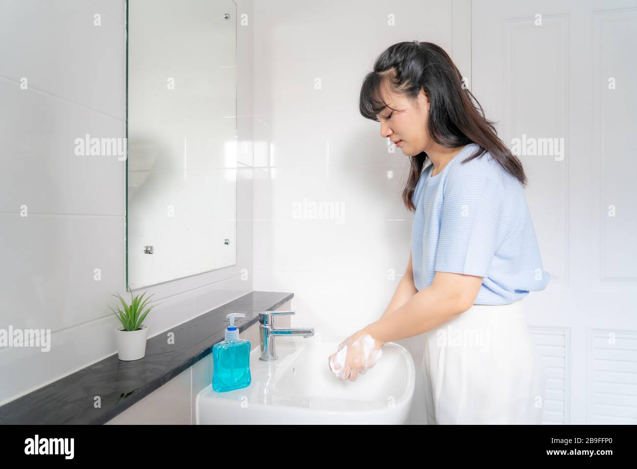 Asian Woman waschen Hände mit Seife unter dem Hahn mit Wasser im Badezimmer zu Hause. Stoppen Sie den Covid-19-Ausbruch. Coronavirus und epidemische Virussymptome. Stockfoto