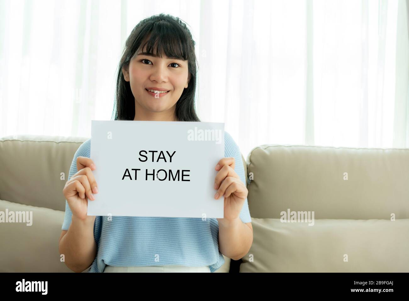 Asian Woman, die ein Blatt Papier mit Text hält, bleibt zu Hause, um Virus zu schützen und kümmert sich um ihre Gesundheit von COVID-19. Bleiben Sie zu Hause. Stockfoto