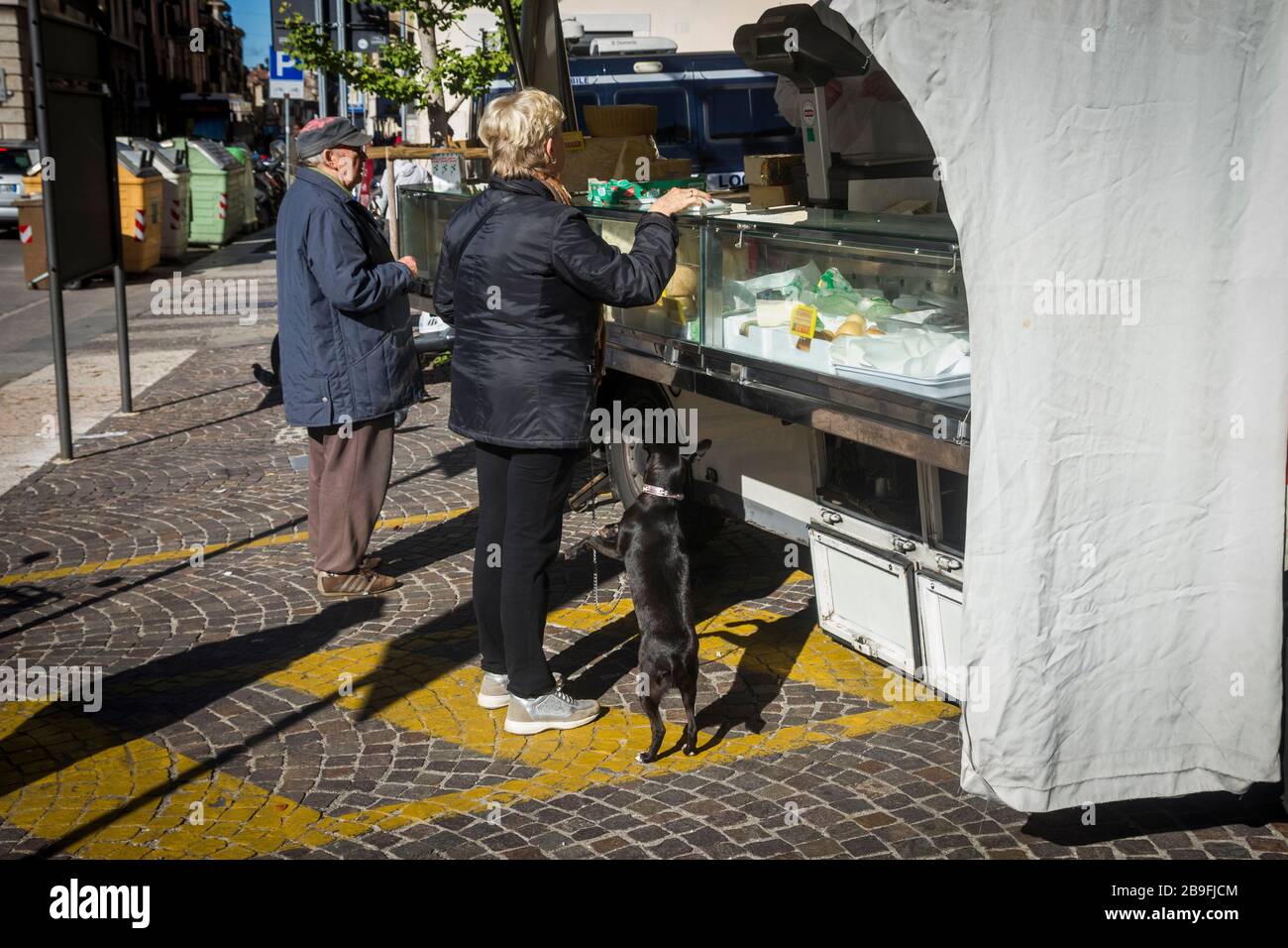 Ein Hund fleht von seinem Besitzer an, der Lebensmittel von einem Marktstand in Verona, Italien, kauft Stockfoto