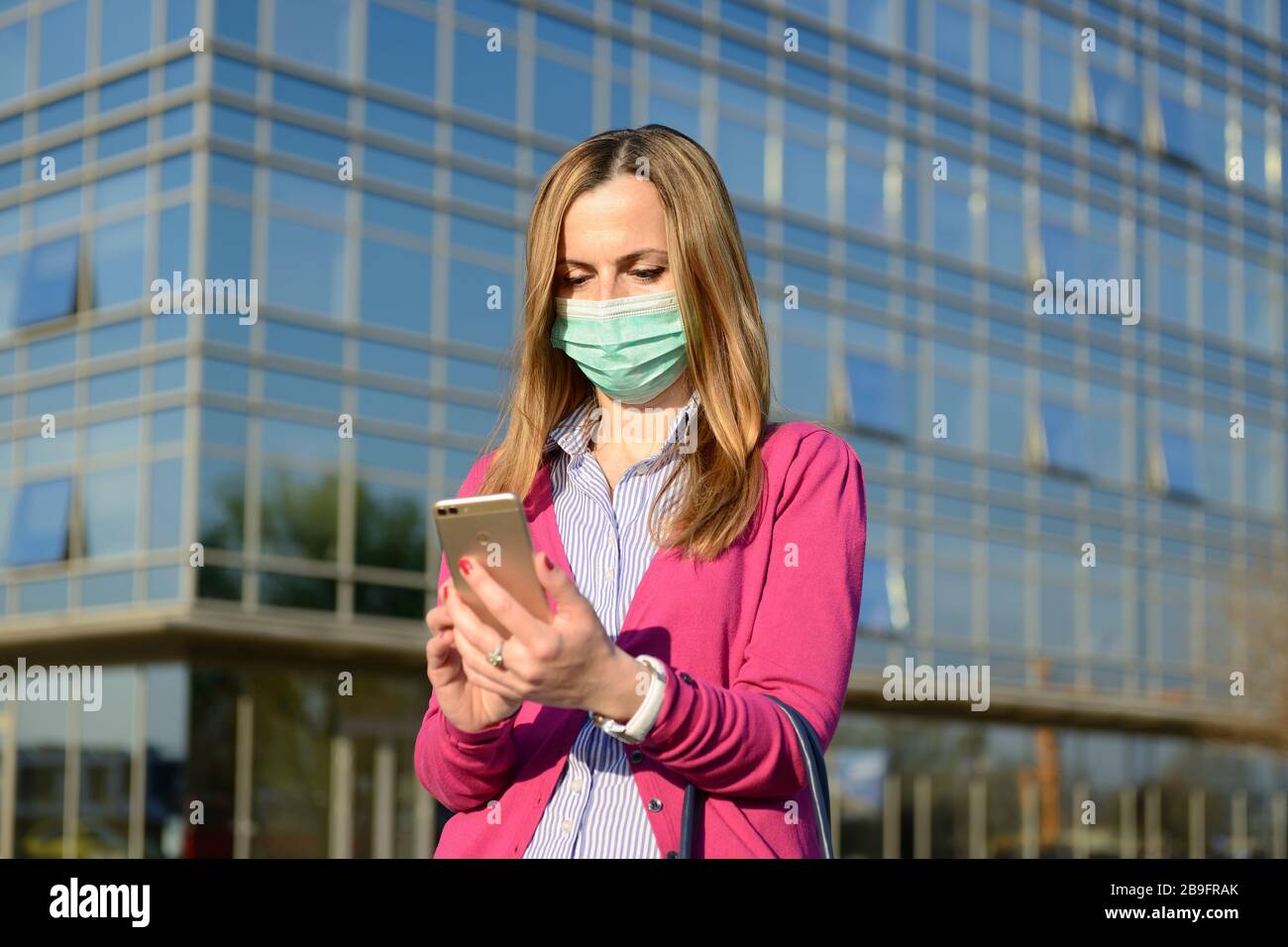 Coronavirus-Epidemie, Frau trägt eine schützende Gesichtsmaske und mit einem Smartphone in einer Stadtstraße als die Zahl der Covid 19 Virusfälle in ganz Europa Stockfoto