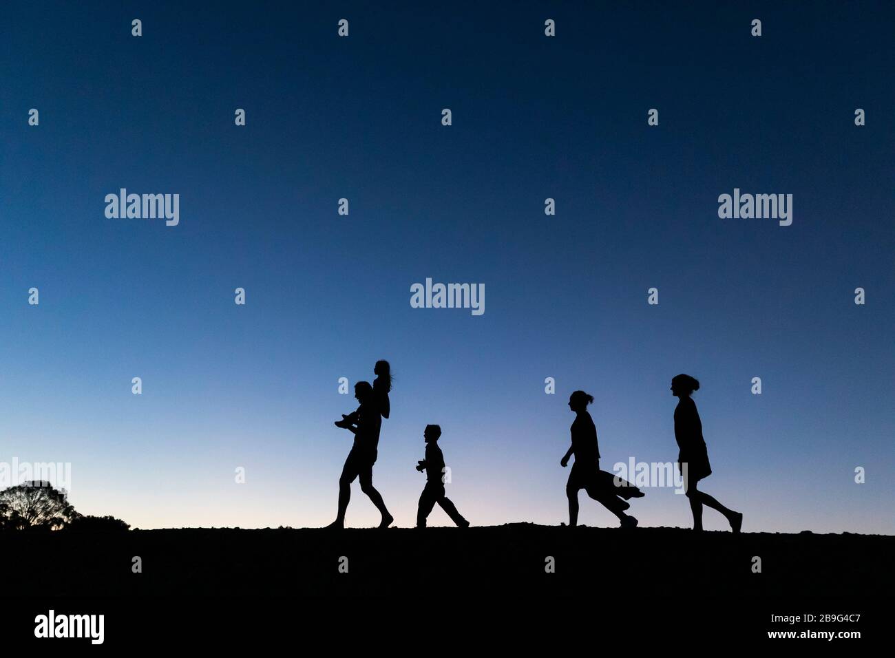 Silhouettenfamilie, die in der Dämmerung gegen den blauen Himmel spazieren geht Stockfoto