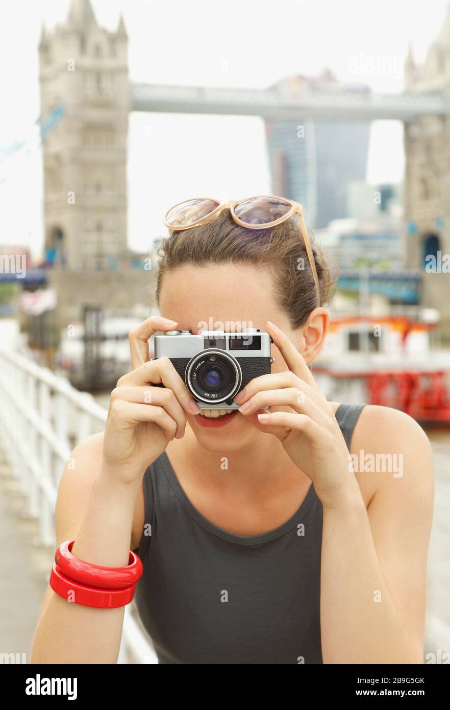 Portrait junge Frau mit Retro-Kamera vor Tower Bridge, London Stockfoto