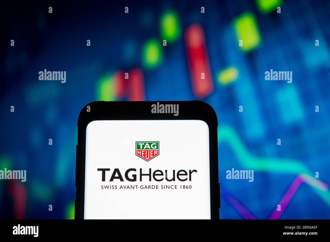 In dieser Abbildung wird ein Tag Heuer Logo auf einem Smartphone angezeigt.ALS Hintergrund WIRD EIN Börsendiagramm angezeigt. Stockfoto