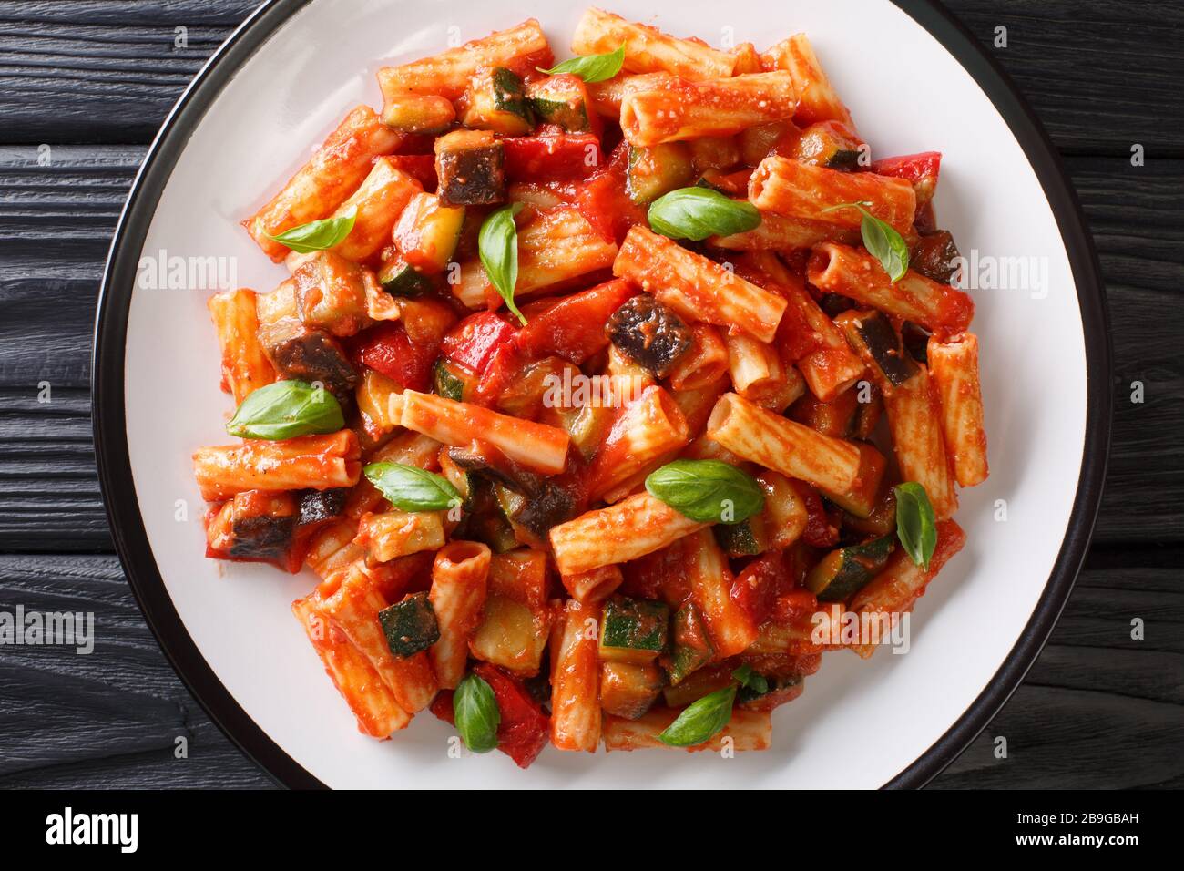 Talian Pasta Tortiglioni mit Auberginen, Zucchini, Pfeffer und Basilikum in Tomatensauce in einer Platte auf dem Tisch. Horizontale Draufsicht von oben Stockfoto