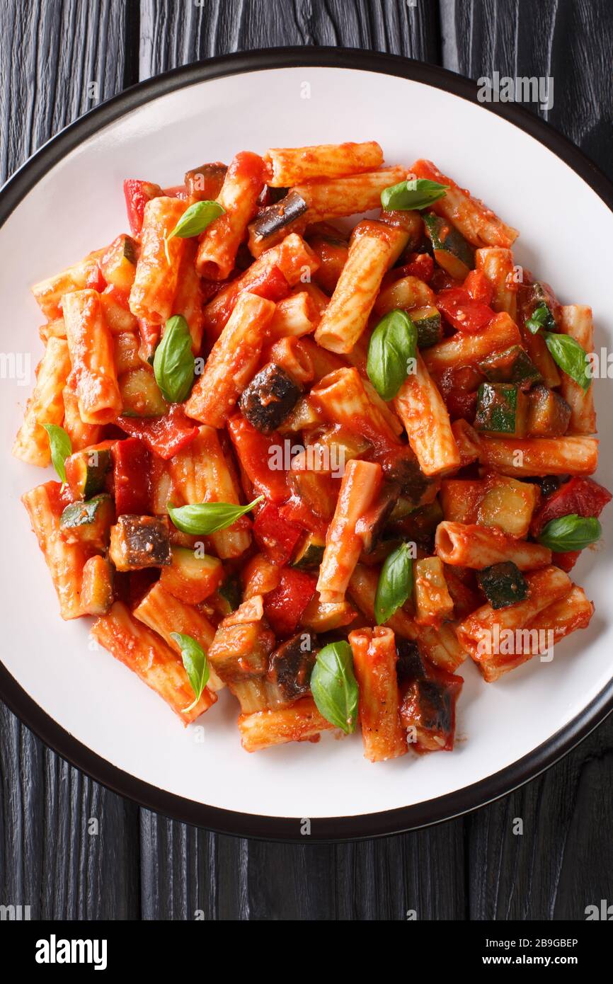 Vegetarische Tortiglioni Pasta mit Gemüse und Basilikum in Tomatensauce in einem Teller auf dem Tisch. Vertikale Draufsicht von oben Stockfoto