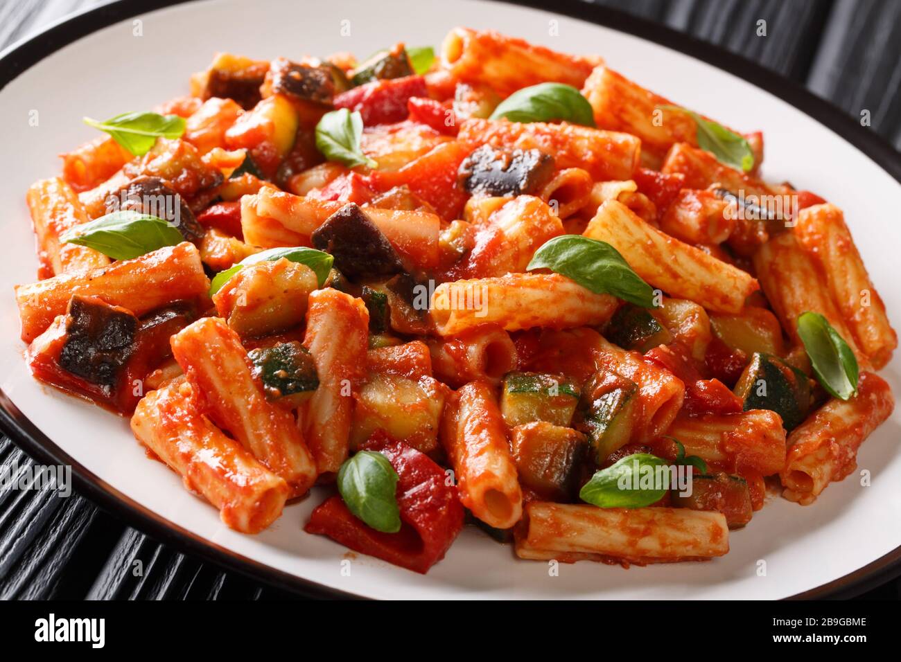 Talian Pasta Tortiglioni mit Auberginen, Zucchini, Pfeffer und Basilikum in Tomatensauce in einer Platte auf dem Tisch. Horizontal Stockfoto