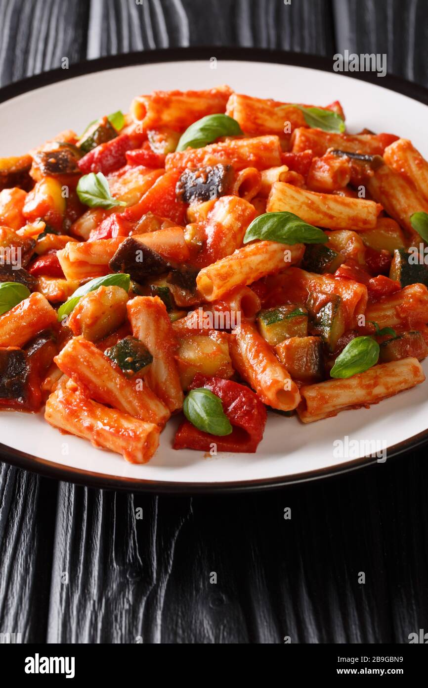 Tortiglioni Pasta mit Auberginen, Zucchini, Pfeffer und Basilikum in Tomatensauce in einem Teller auf dem Tisch. Vertikal Stockfoto