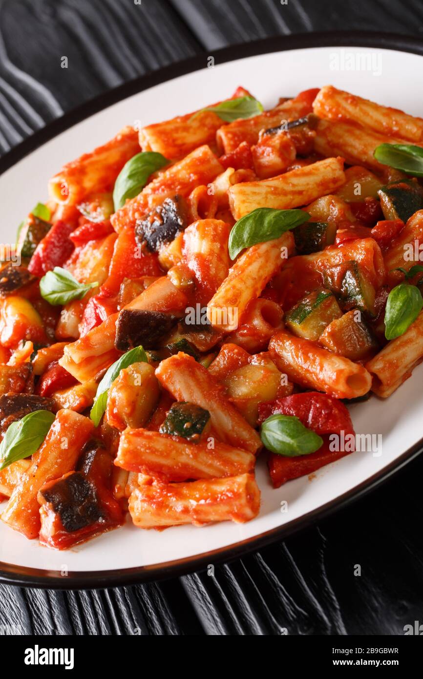 Vegetarische Tortiglioni Pasta mit Gemüse und Basilikum in Tomatensauce in einem Teller auf dem Tisch. Vertikal Stockfoto