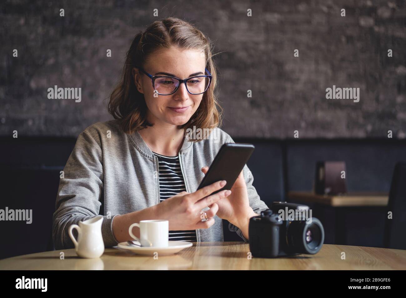 Junge Frau, die mit ihrem Handy in einer Cafeteria sitzt Stockfoto