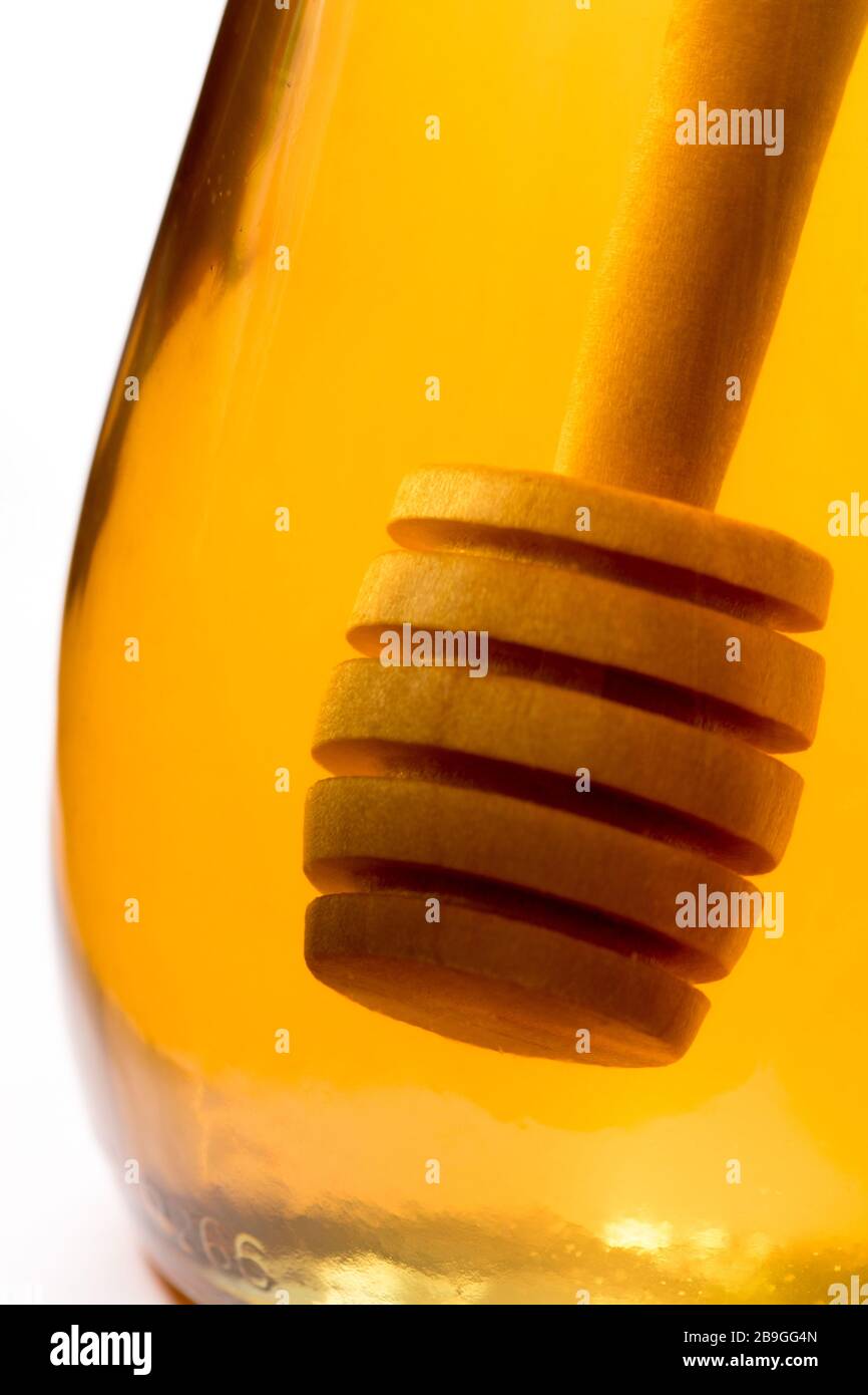 Ein hölzerner Honigtriesler tauchte in ein Glas klaren Honigs zurück beleuchtet durch goldenes transparentes Licht. Stockfoto