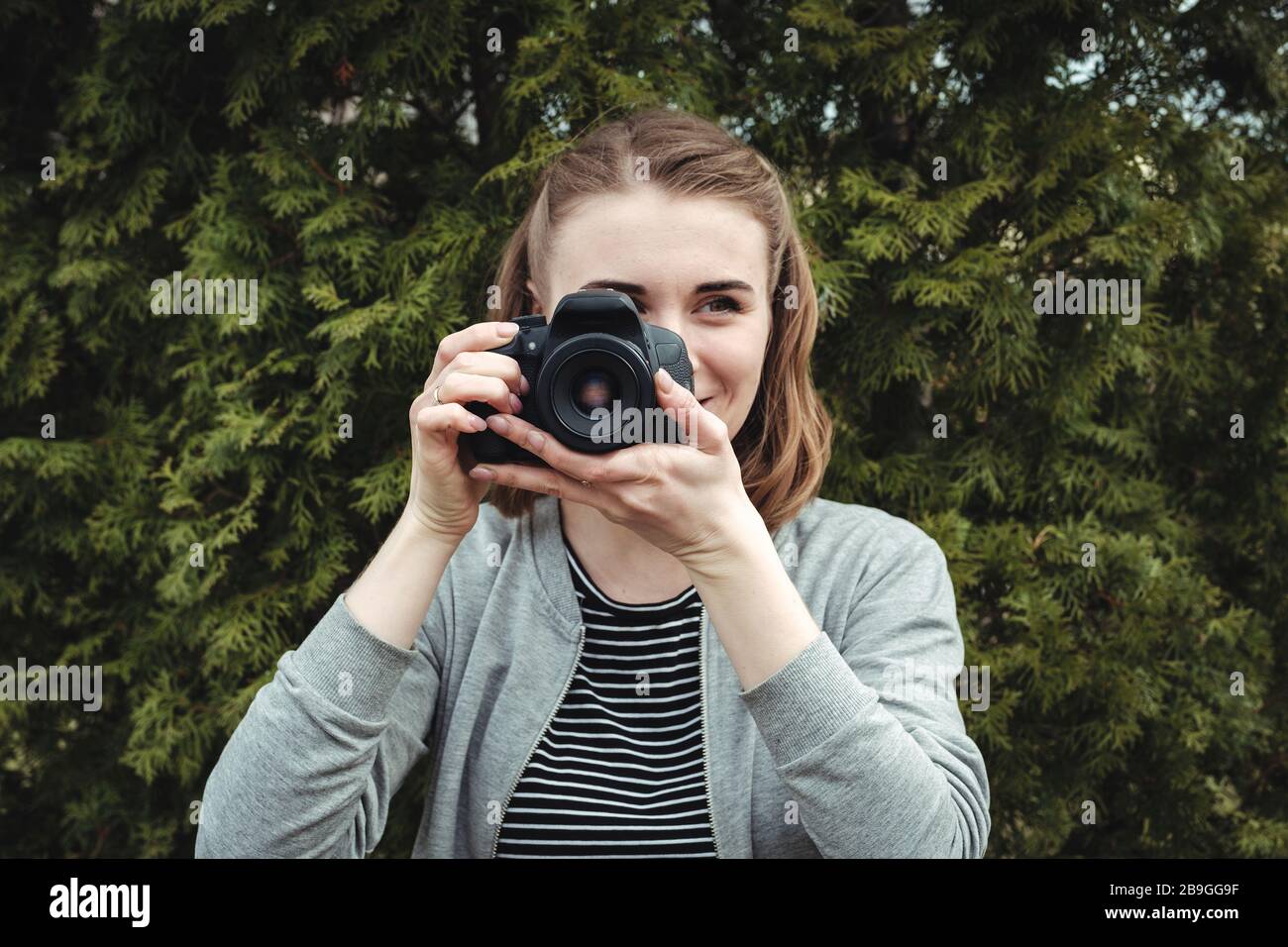 Junge Frau, die im Freien fotografiert und dabei auf eine Kamera fokussiert Stockfoto