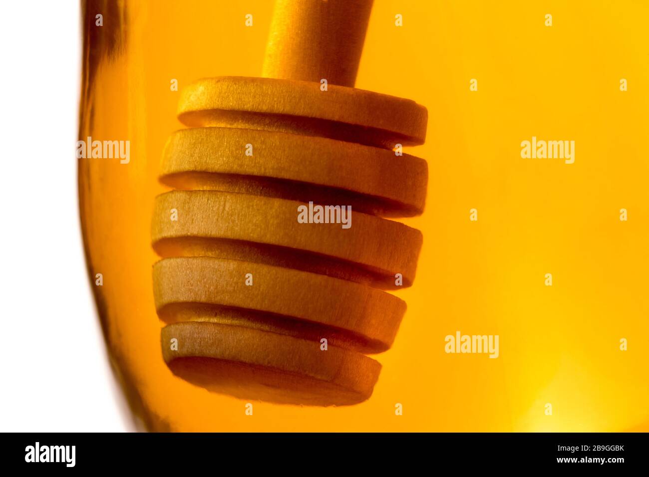 Ein hölzerner Honigtriesler tauchte in ein Glas klaren Honigs zurück beleuchtet durch goldenes transparentes Licht. Stockfoto