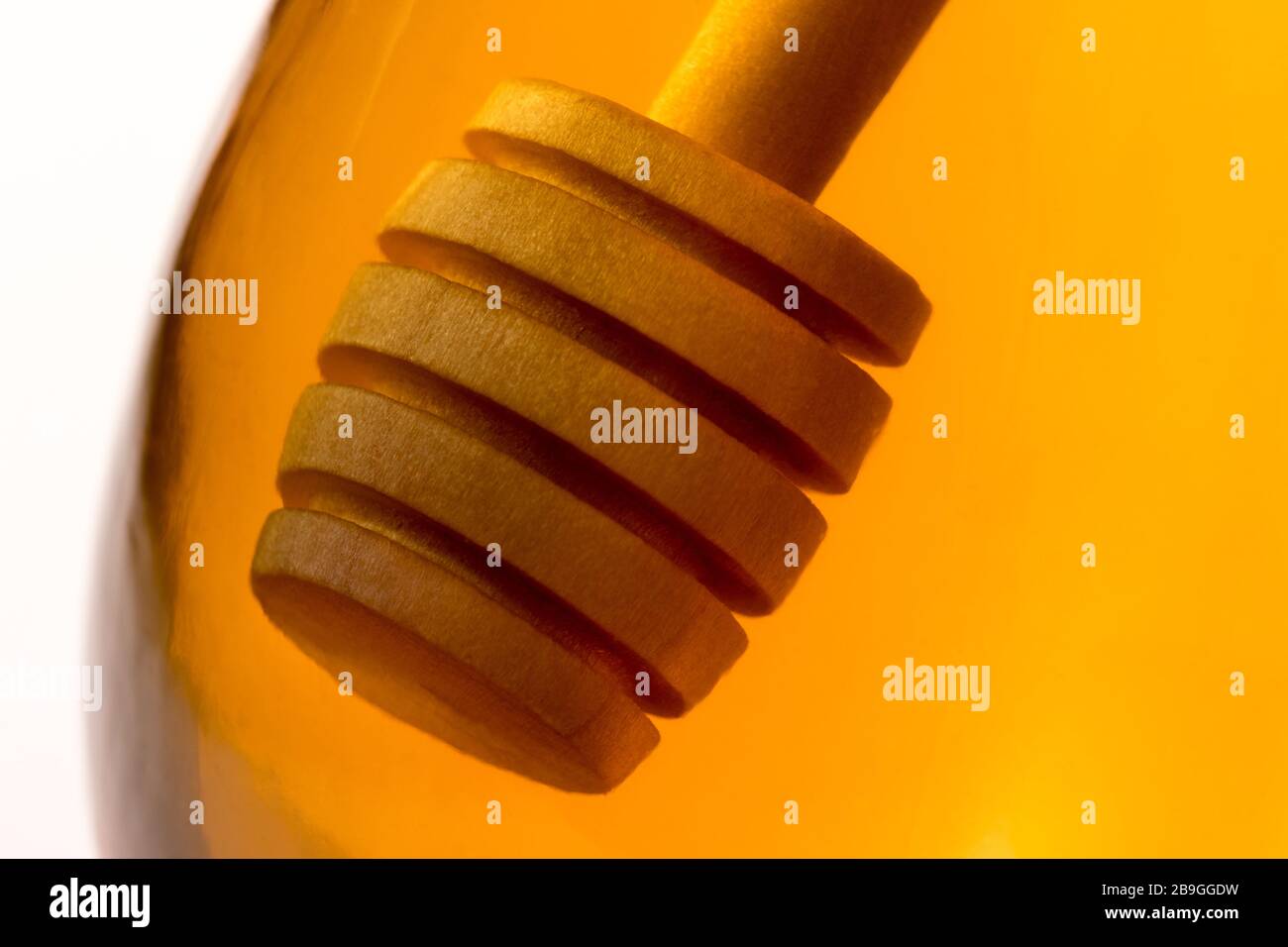 Ein hölzerner Honigtriesler tauchte in ein Glas klaren Honigs zurück beleuchtet durch goldenes transparentes Licht. Stockfoto