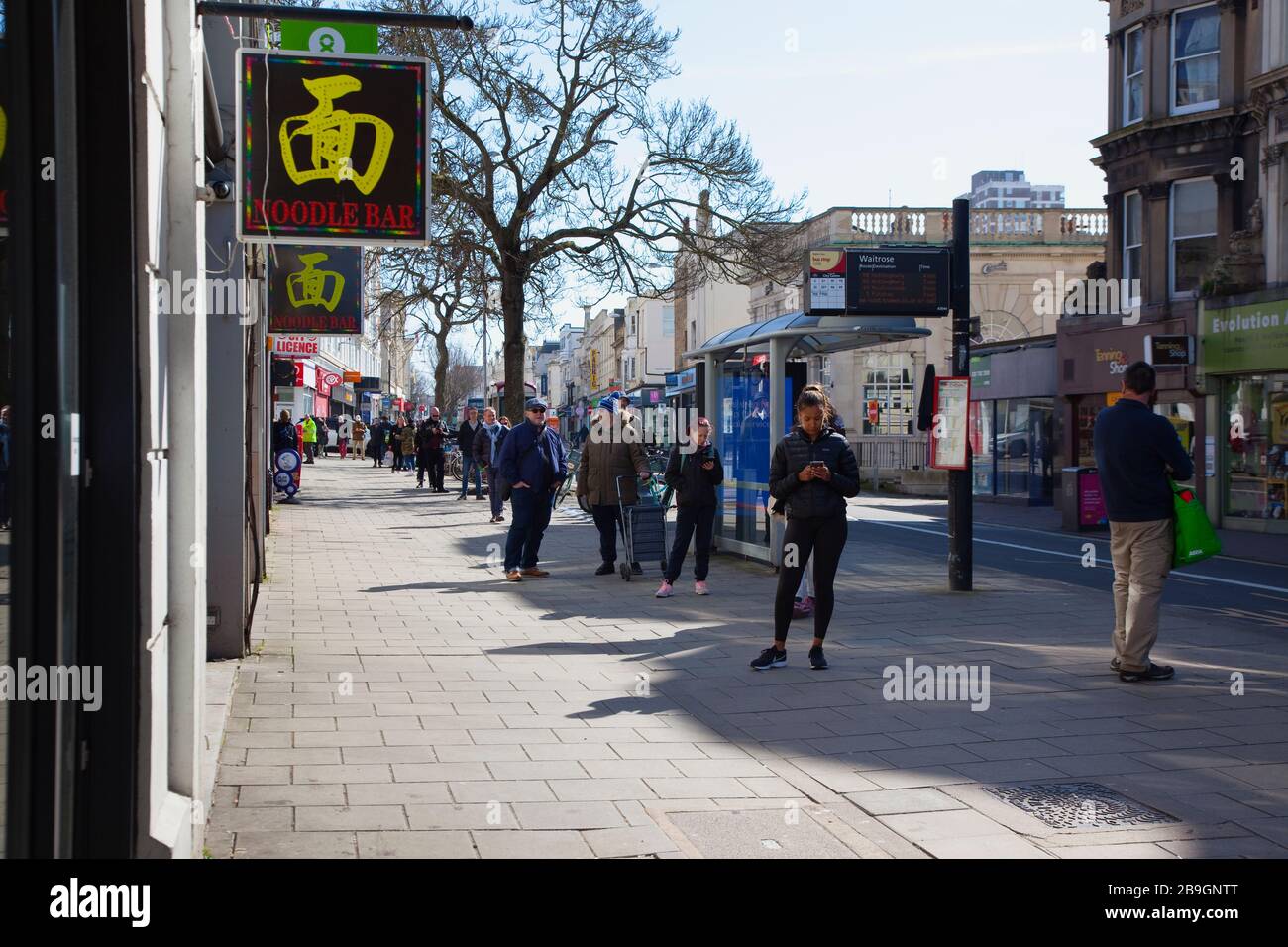 England, East Sussex, Brighton, Menschen in der Warteschlange mit sozialen Distanzierungsmaßnahmen, die von Waitrose Supermarket eingeführt wurden, um Menschen zu begrenzen, die in den Laden eindringen. Stockfoto