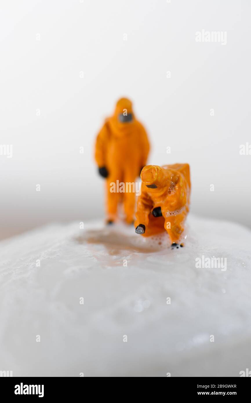 Konzeptbild für Coronavirus mit Miniaturmenschen auf einer Seifenleiste in Haselmatt-Anzügen, die auf Bakterien getestet werden. Stockfoto