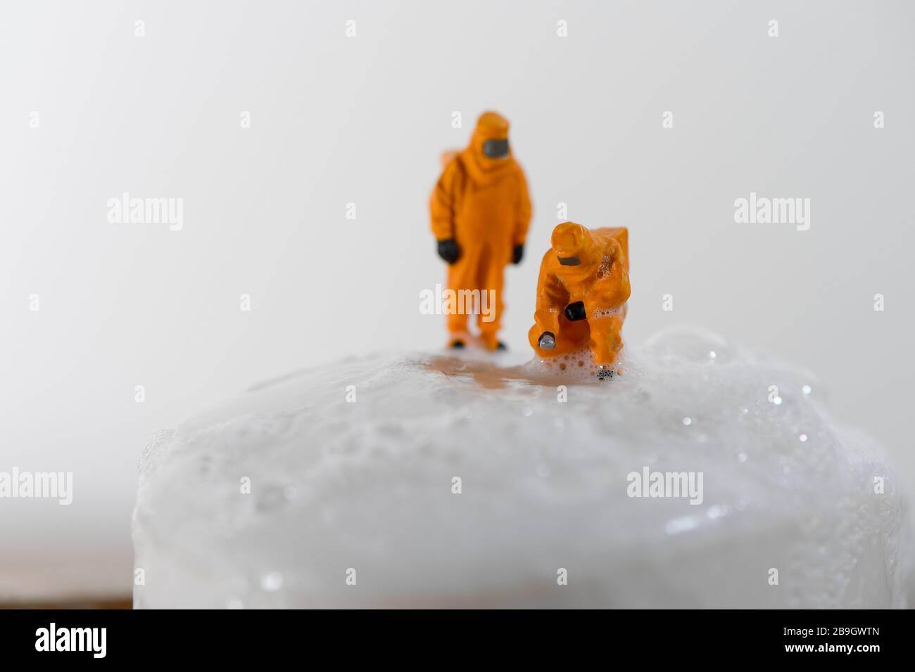 Konzeptbild für Coronavirus mit Miniaturmenschen auf einer Seifenleiste in Haselmatt-Anzügen, die auf Bakterien getestet werden. Stockfoto