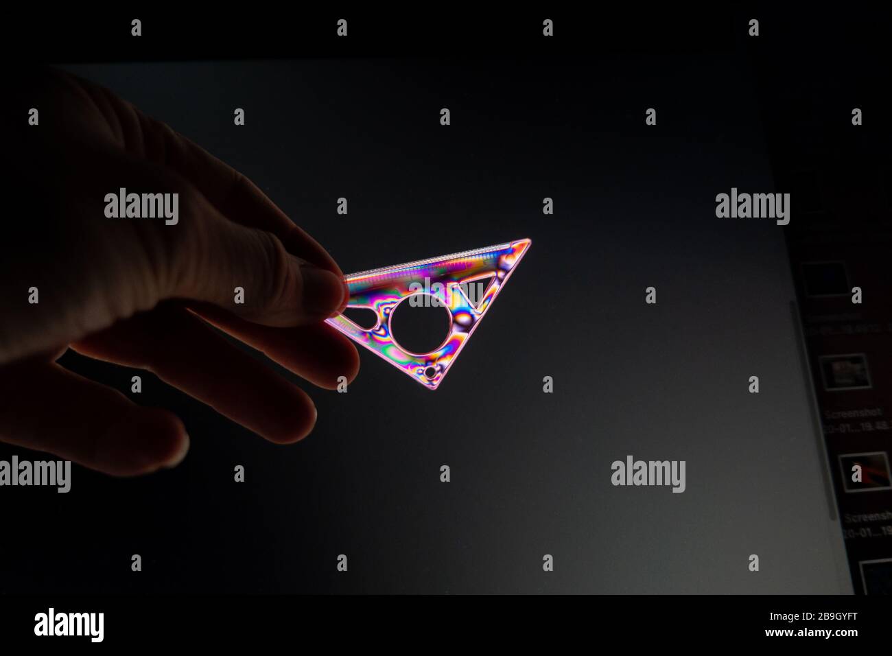Person, die Kreuzpolarisation mit einem transparenten Kunststoff-Set-Quadrat demonstriert, fotografiert durch einen Polarisationsfilter mit polarisierter Lichtquelle. Stockfoto