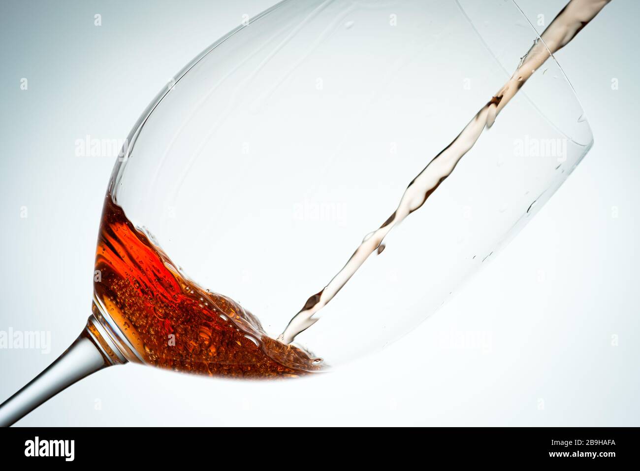 Rotweinglas mit strömender Flüssigkeit in Hintergrundbeleuchtung Stockfoto