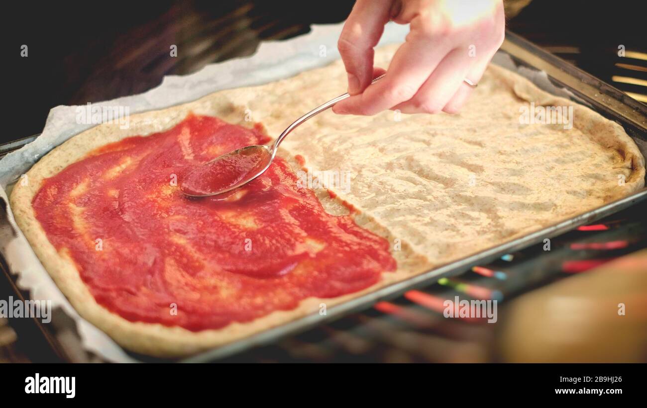 Die Hände verteilen Tomatenpüree mit Löffel auf Bakinblech - hausgemachte rustikale Pizza italienischer Kochgrund Stockfoto