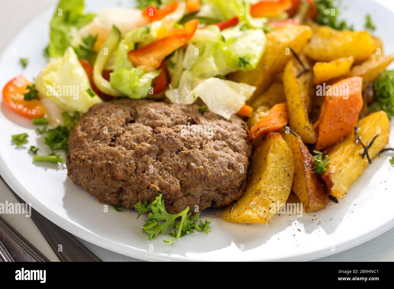 Leckeres Rindfleisch Burger Patty mit Salatgarnierung und Kartoffelspalten Stockfoto