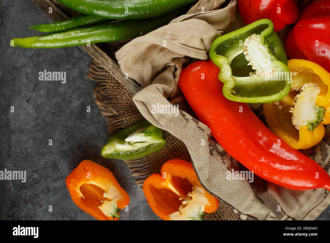 Ganz- und halbgeschnittene Paprika in einem rustikalen Tablett. Draufsicht. Stockfoto