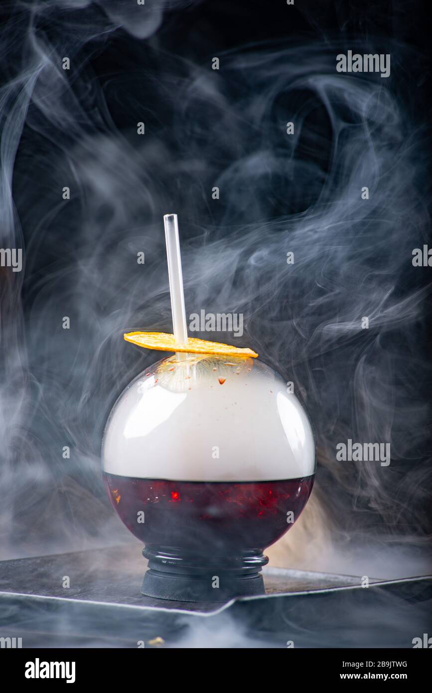 Kugelglas mit Rauch und Alkohol. Karamellisierte Zitronenscheiben. Rauch auf schwarzem Hintergrund. Stockfoto