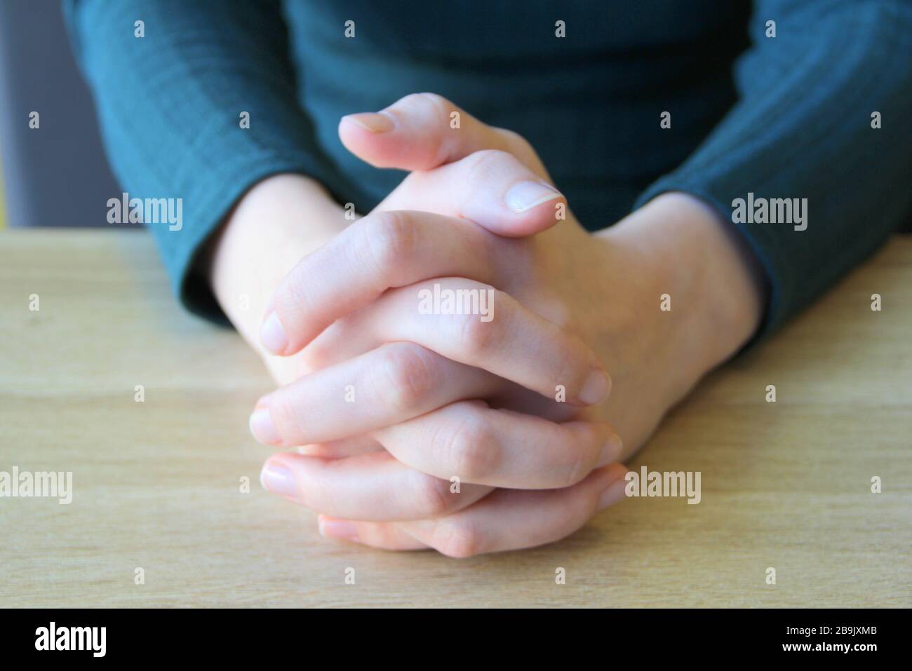 Im Gebet gefaltete Handflächen. Eingeklemmte Finger. Das Mädchen sitzt und hält die Hände vor den zusammengeklemmten Händen. Stockfoto