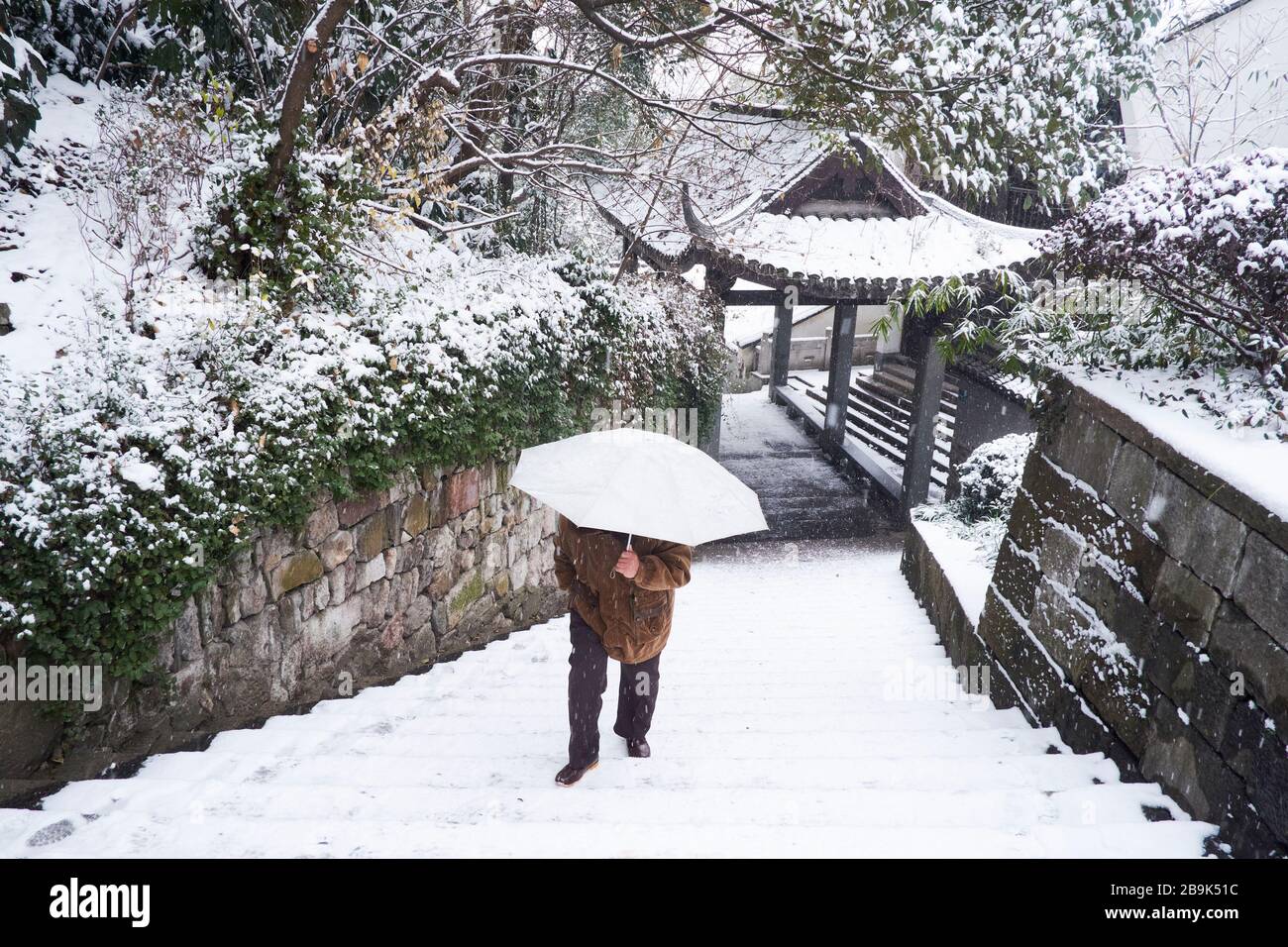 Ein Mann, der mit einem Regenschirm im Schnee in Hangzhou, China, spazieren geht Stockfoto