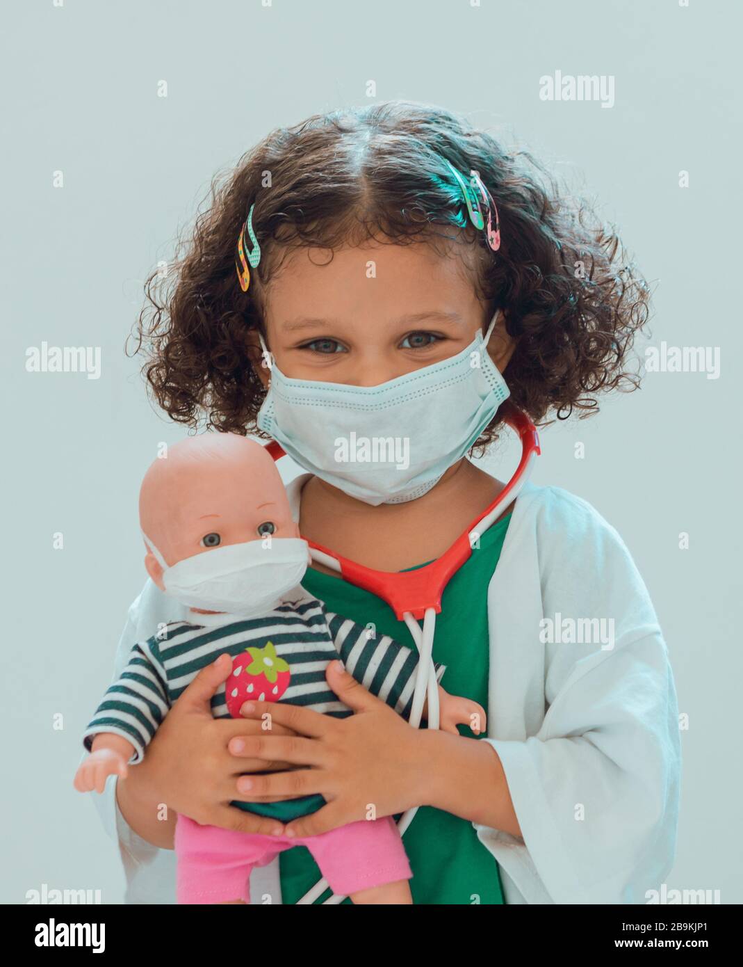 Ein kleines Mädchen, das den Arzt spielt, umarmt ihre Patientin, sie tragen alle Schutzmasken Stockfoto