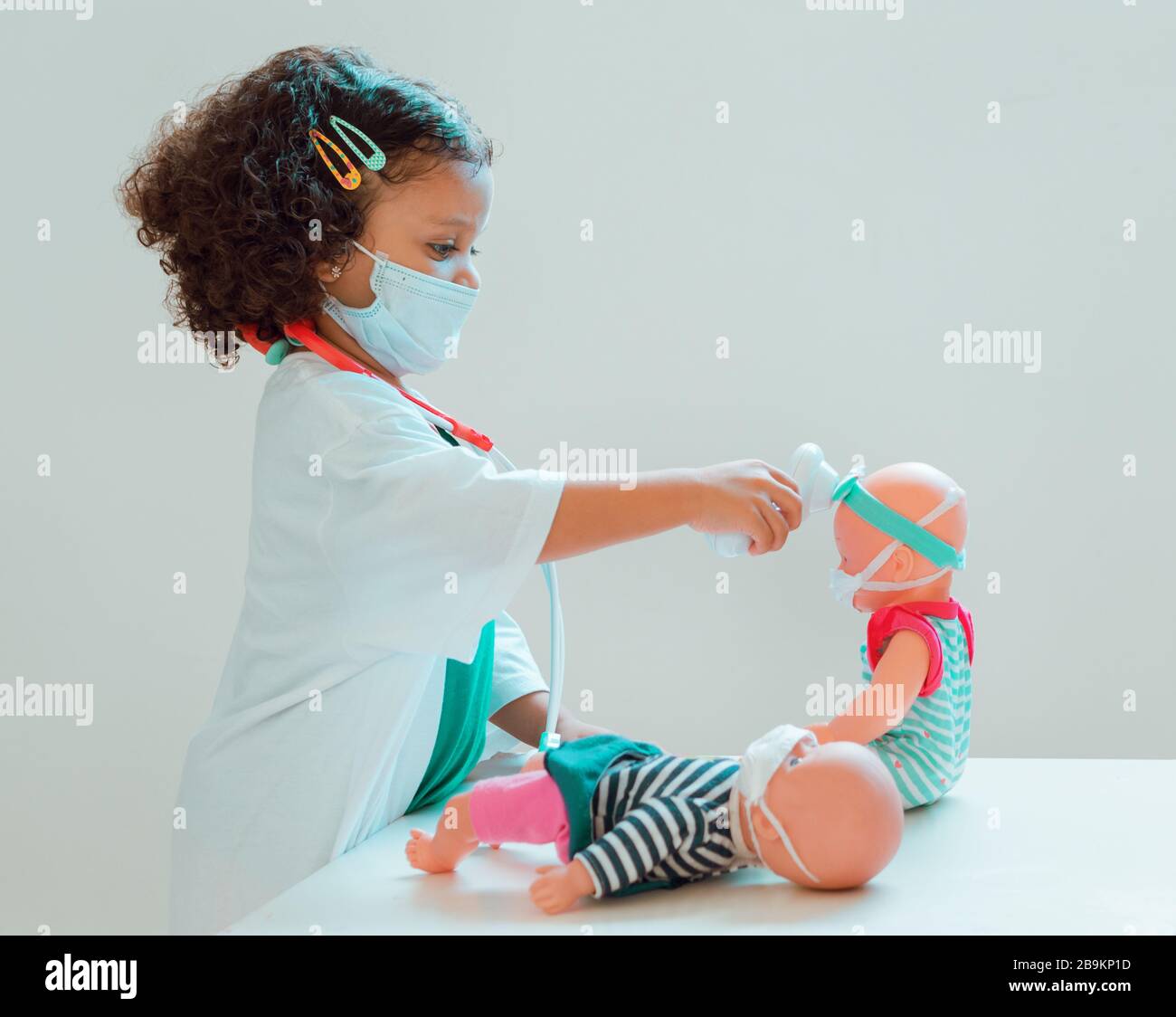 Ein kleines Mädchen, das den Arzt spielt, misst das Fieber ihrer Patientin, jeder trägt Schutzmasken Stockfoto