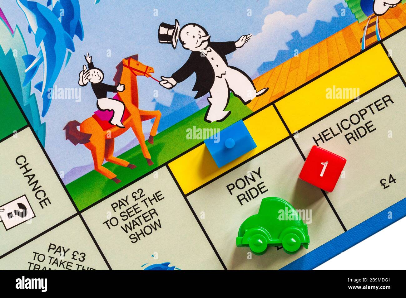 Junior Monopoly-Brettspiel - Detail des grünen Auto-Tokens auf Pony-Ride-Platz mit Haus und roten Würfeln, die 1 zeigen Stockfoto