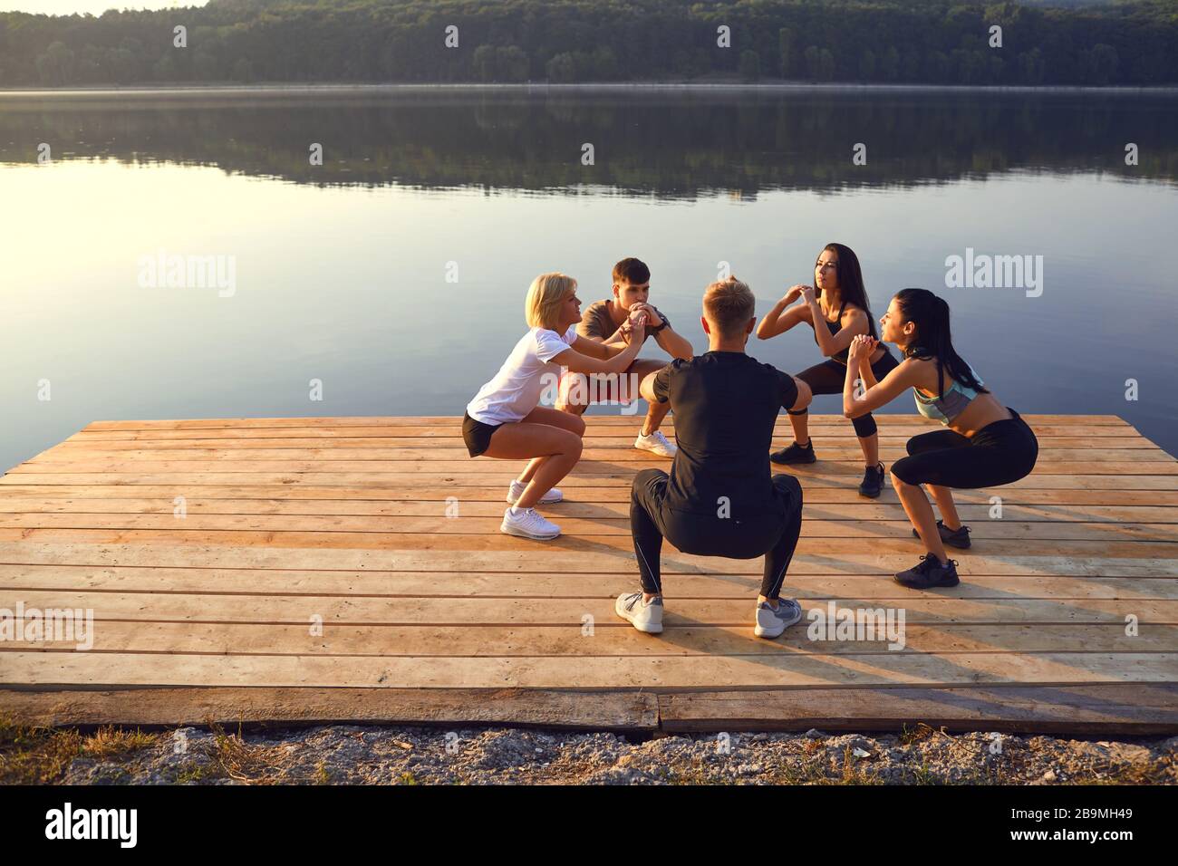 Eine Gruppe von Sport Leute tun Hocke Übungen in einem Park am See Stockfoto