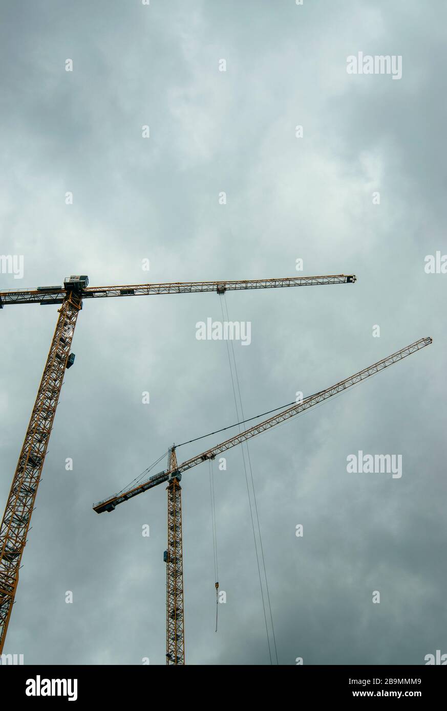 Zwei Baukräne gegen einen grauen Himmel, von unten betrachtet Stockfoto