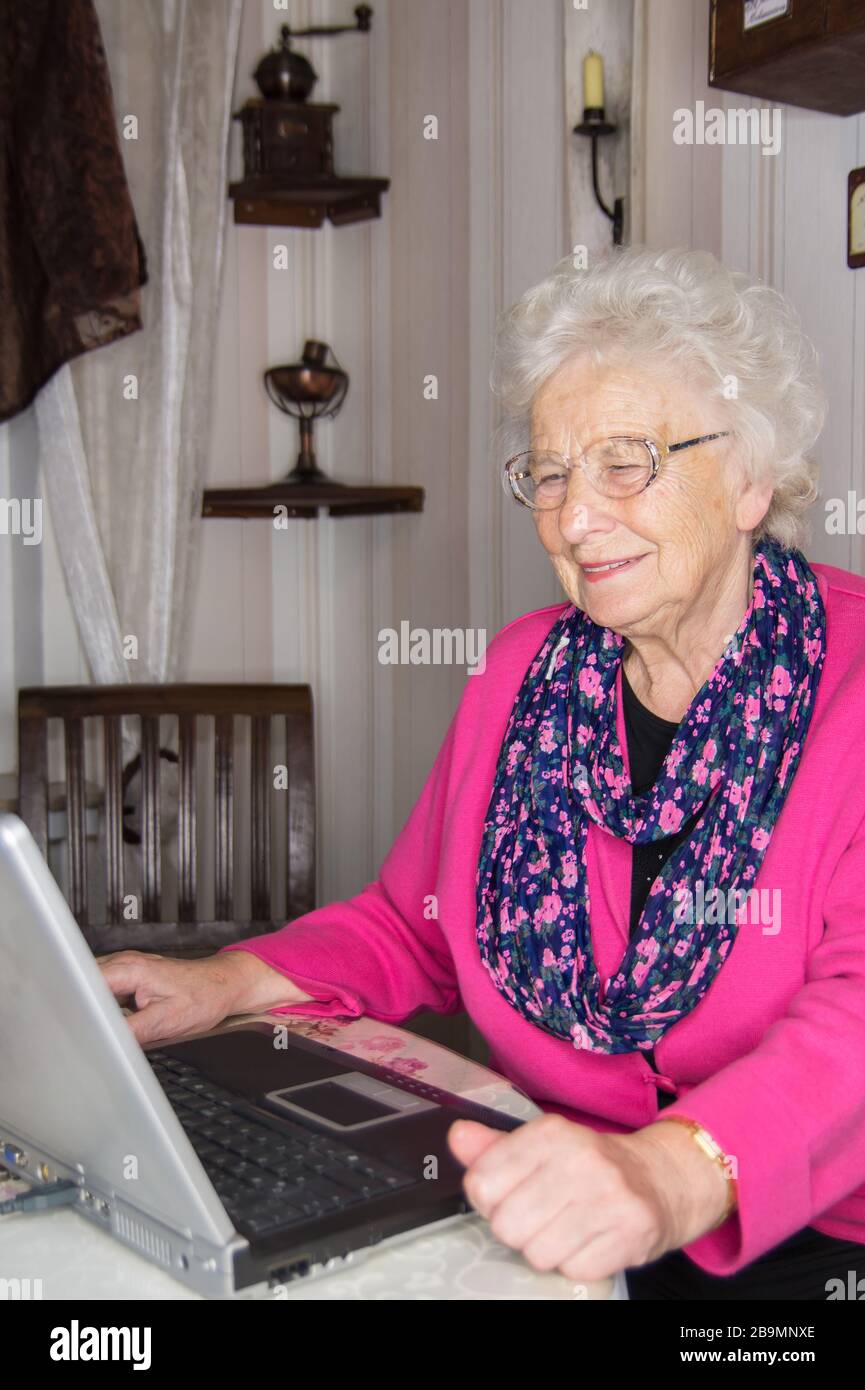 80 Jahre alte Frau allein zu Hause. Sie gehört der Risikogruppe für Covid 19 an. Die ältere Frau schreibt auf dem Laptop gegen die Isolation mit ihrer Familie Stockfoto