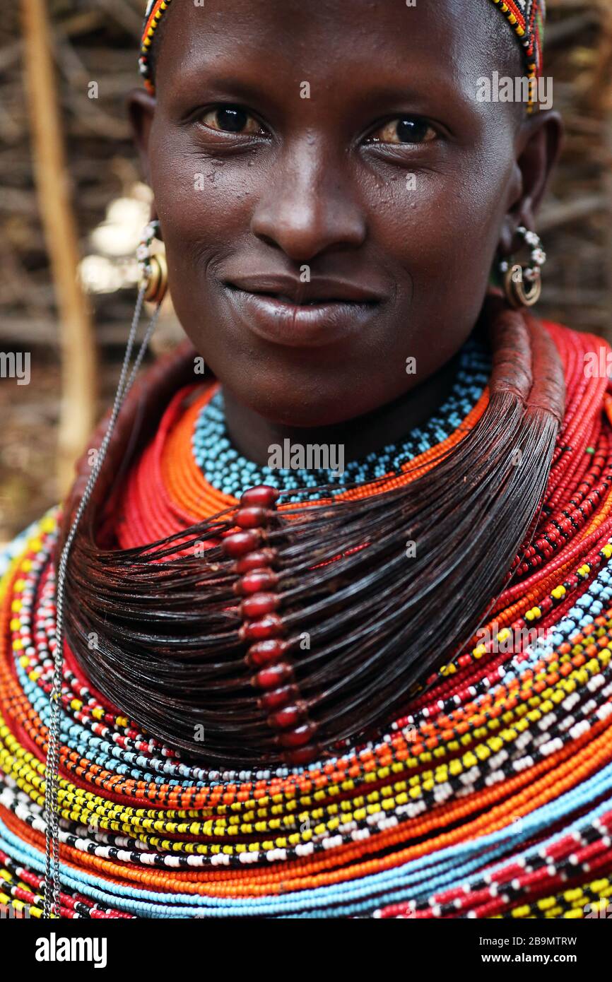 Eine junge Samburu-Frau, die in traditioneller Kleidung lächelt, in einem abgelegenen Samburu-Stammdorf in der Nähe von South Horr, Kenia. Stockfoto