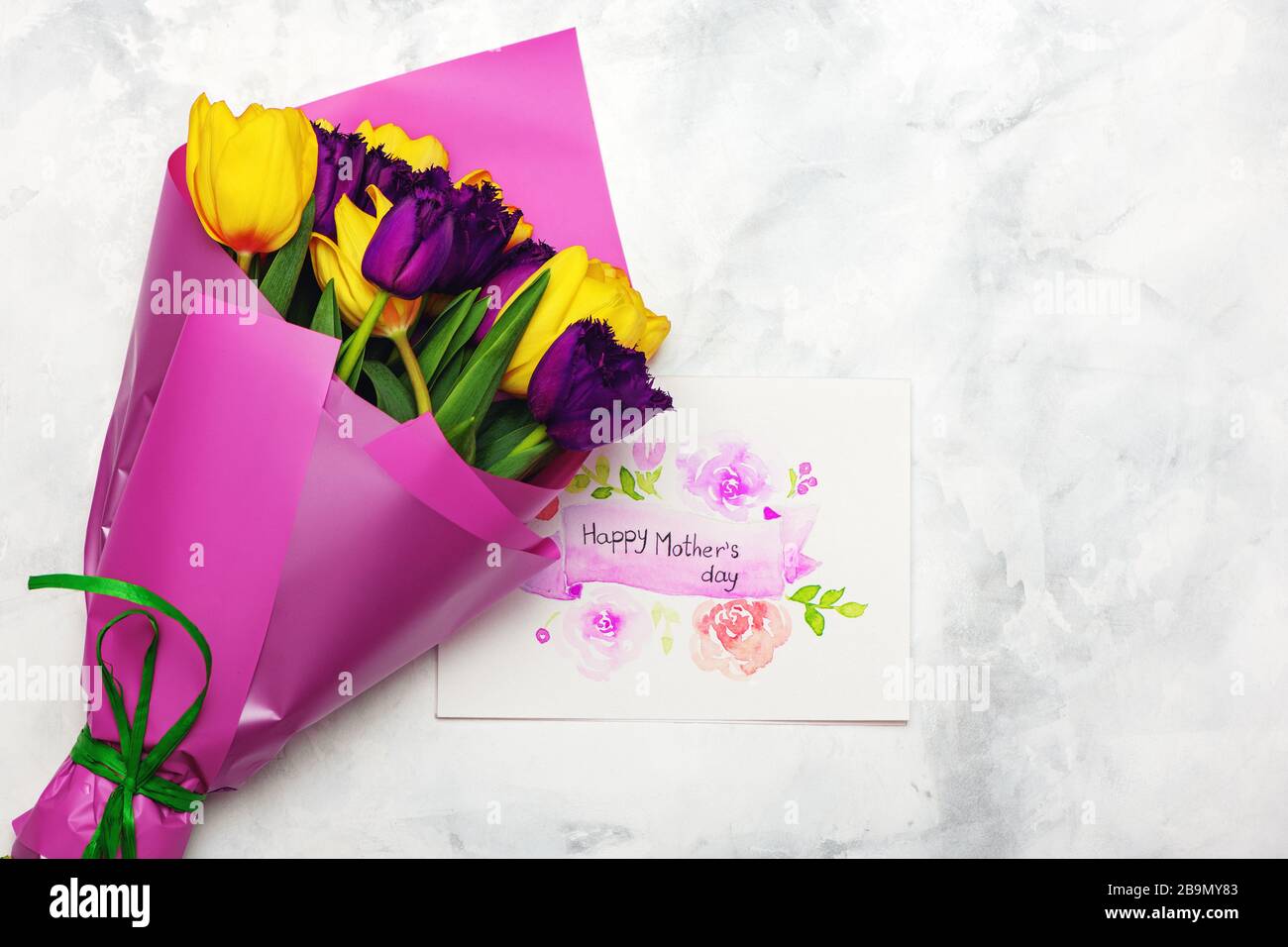 Farbenfroher Blumenstrauß mit frischen Tulpen mit Kunsthandwerkspostkarte auf weißem Marmorhintergrund. Tageskonzept der Mutter. Stockfoto