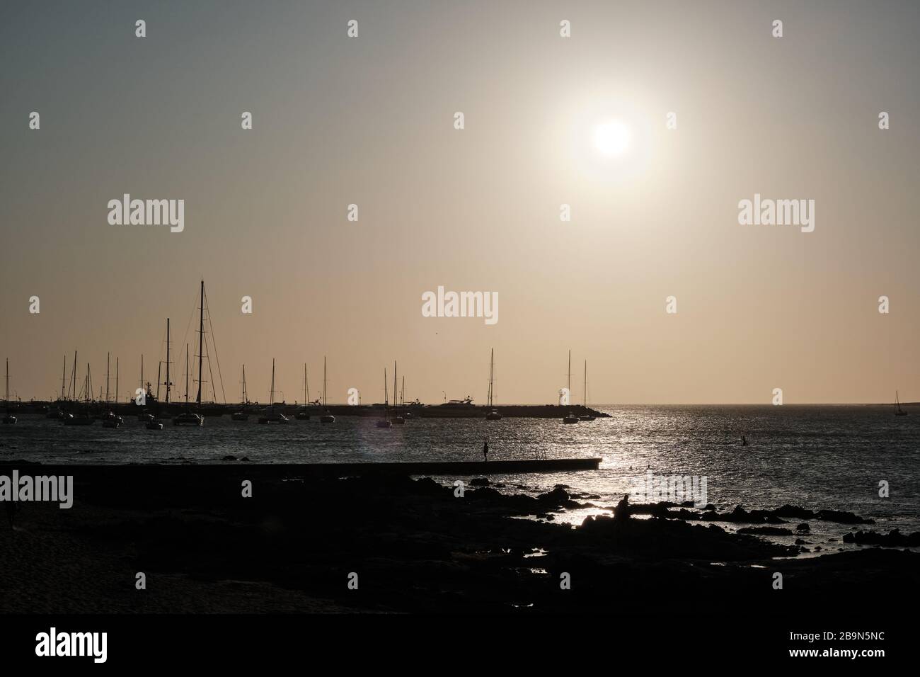 Blick auf den Sonnenuntergang im atlantischen Meer hinter den Booten und Segeln von den Felsen des Hafen von Punta del Este, Maldonado, Uruguay Stockfoto