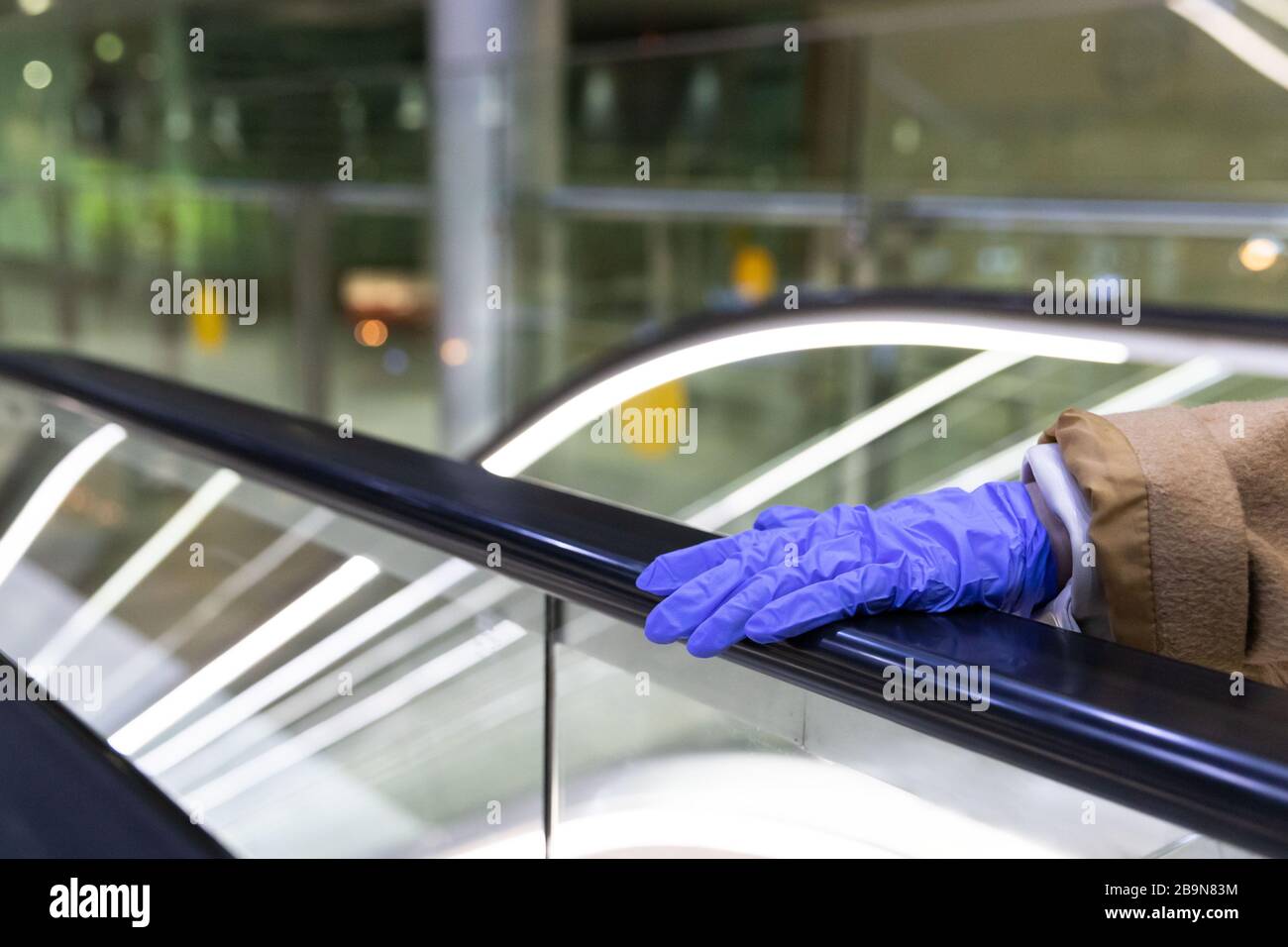 Frau Hand hält Rolltreppe Handlauf im Flughafenterminal durch Latexhandschuhe, um sich vor Kontakt mit Keimen, Viren, Coronavirus/covi zu schützen Stockfoto