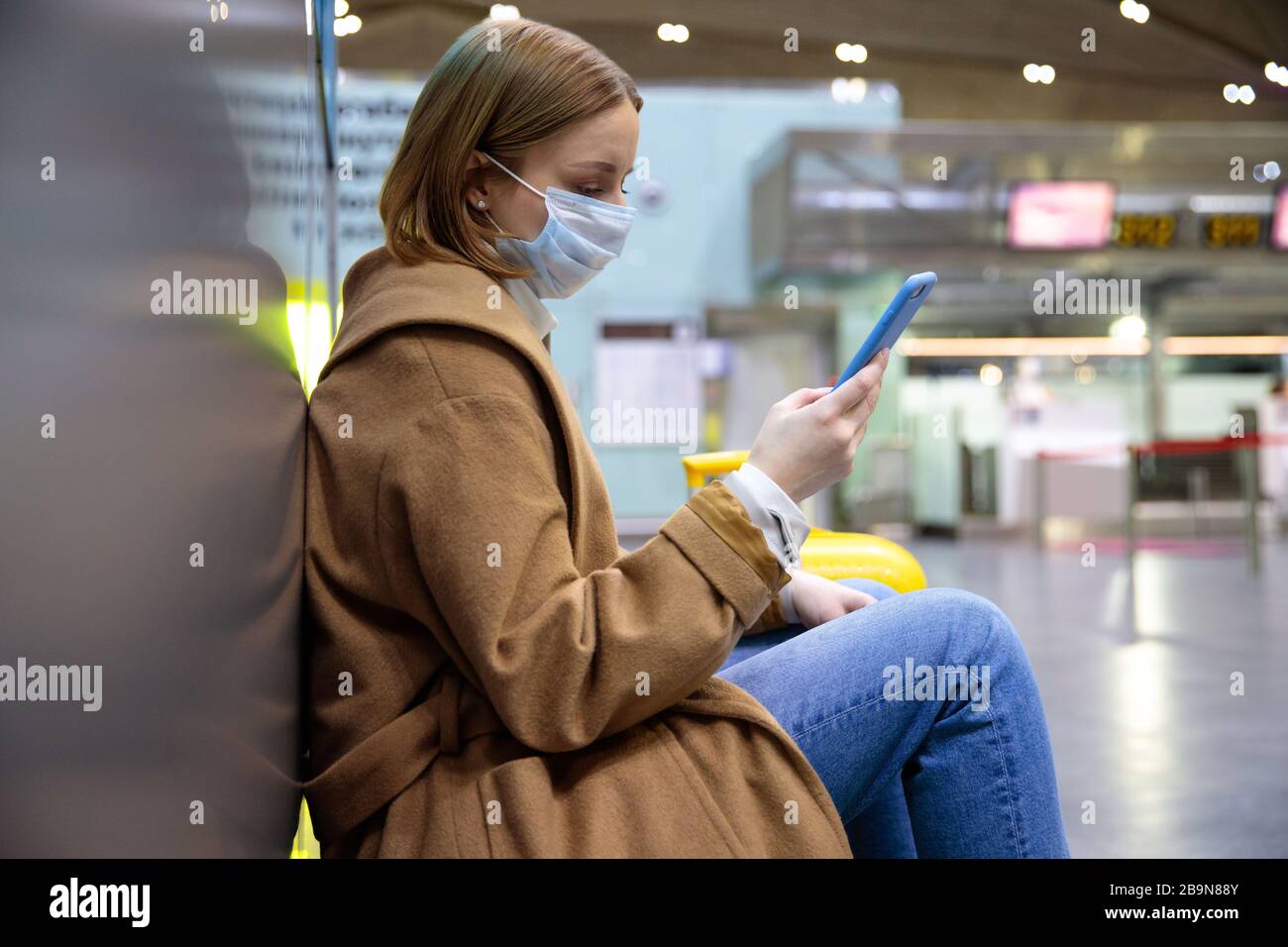 Frau verärgert über die Flugannullierung, schreibt Nachricht an Familie, sitzt in fast leerem Flughafenterminal wegen Coronavirus-Pandemie/Covid-19-Ausbruch Stockfoto