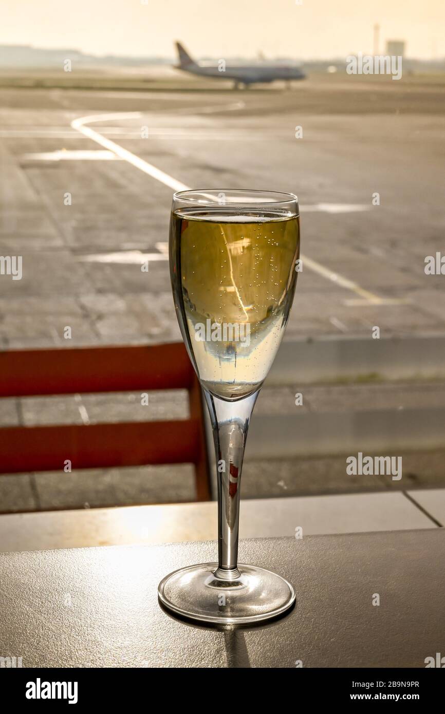 Ein Glas Champagner auf einem Tisch in einer Flughafenlounge mit einem Flugzeug, das im Hintergrund platzt Stockfoto