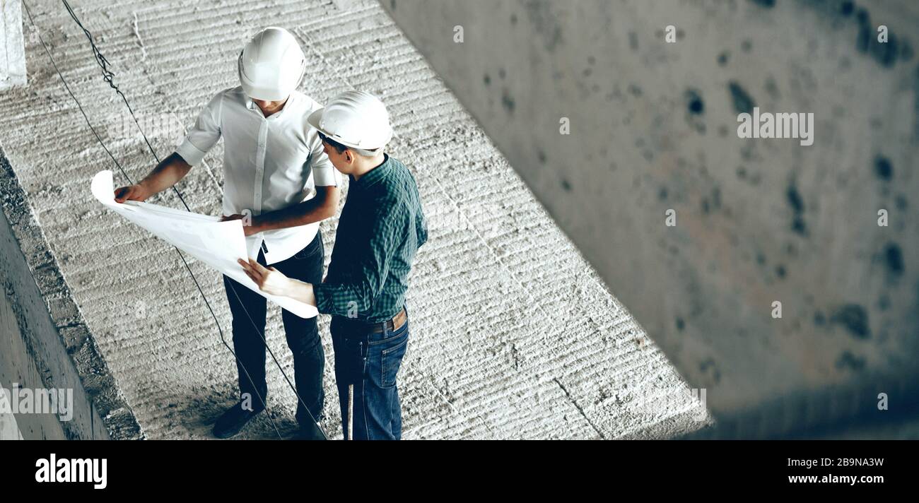 Zwei Erwachsene professionelle Konstrukteure diskutieren über den zukünftigen Bauplan und halten gleichzeitig ein großes Blatt Papier Stockfoto