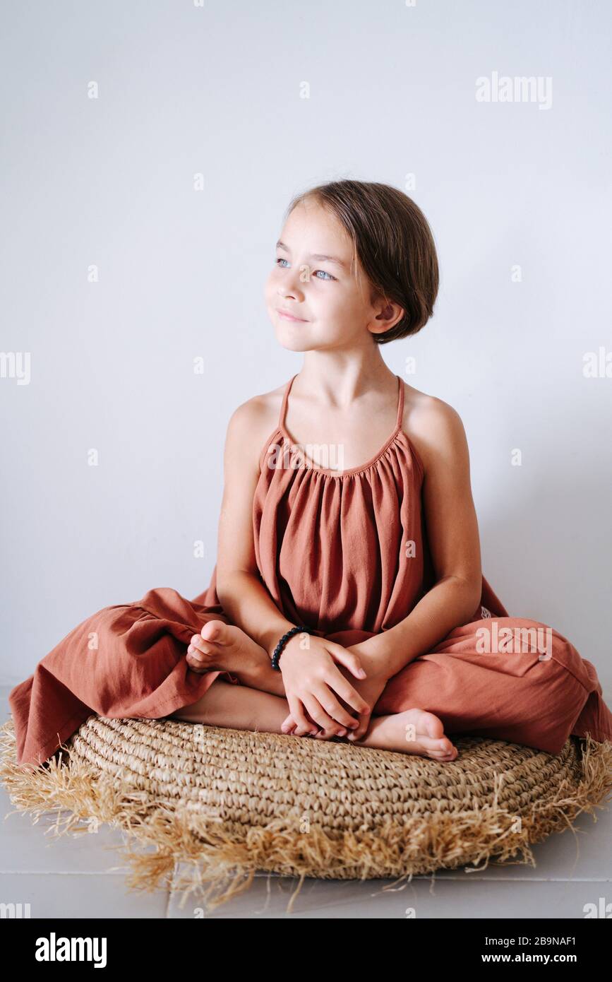 Heiteres kleines Mädchen in einem Kleid, das auf einem Kissen in einem Raum im tropischen Stil meditiert Stockfoto